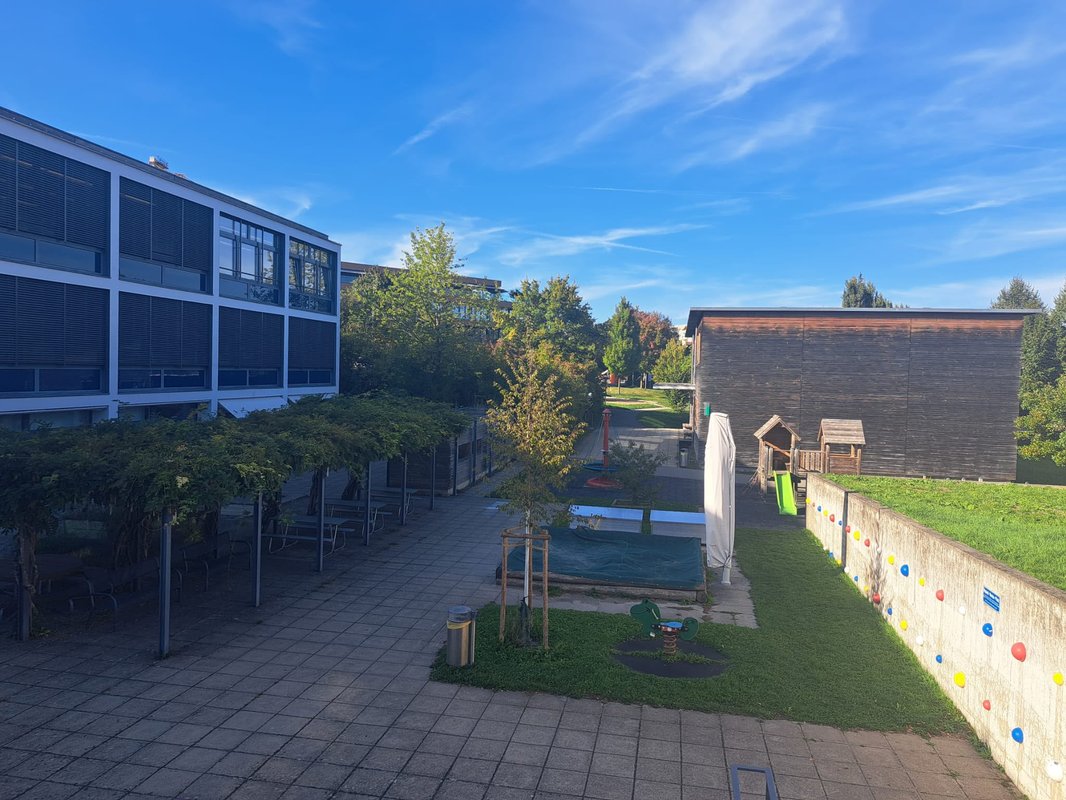 Schoolyard with pergola, sandbox and playground between the school buildings