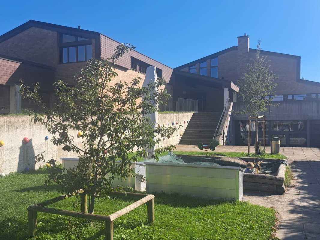 Playground with sandbox and climbing wall in front of the school building